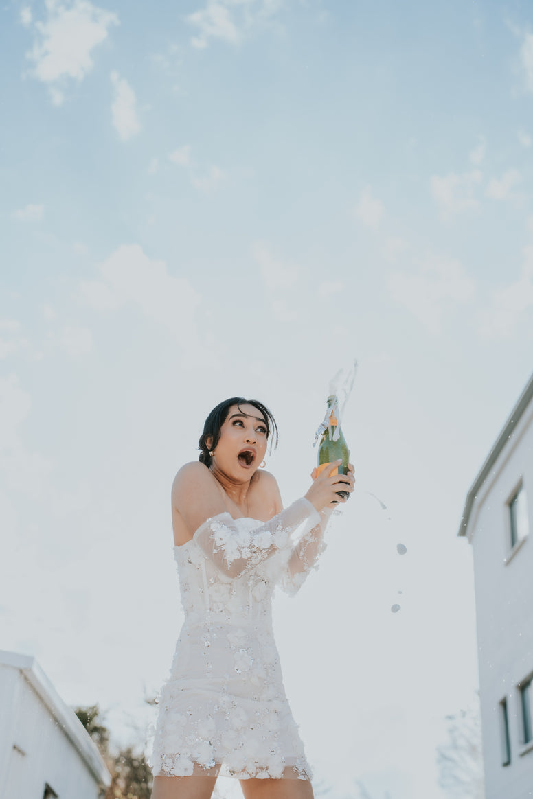 Woman in Saskia white lace dress with champagne